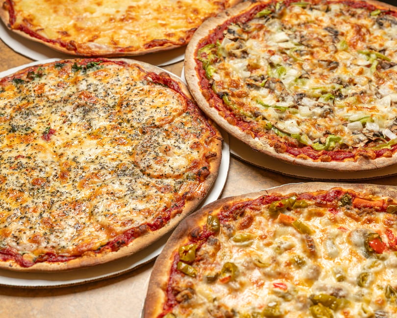Four delicious pizzas with various toppings, including cheese, vegetables, and herbs, on a table.