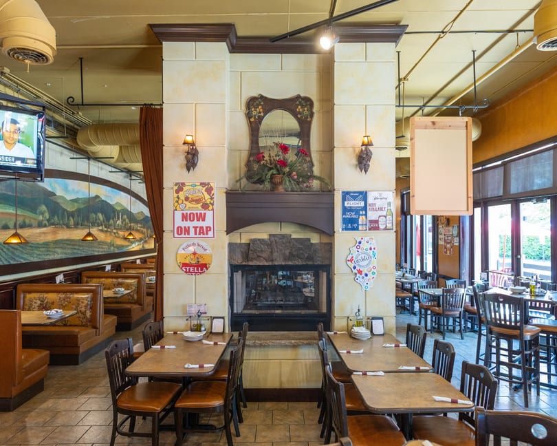 Restaurant interior with a fireplace, booths, tables, chairs, and a large mural on the wall.