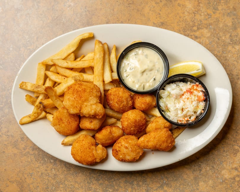 Fried scallops and french fries with tartar sauce, coleslaw, and a lemon wedge.