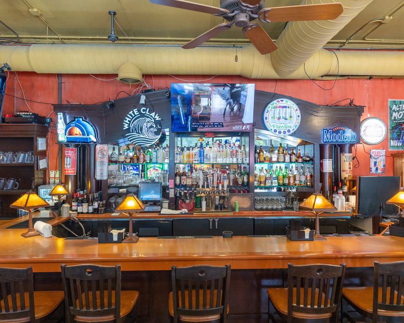 A well-stocked bar with various liquor bottles, beer taps, and bar stools under a ceiling fan.