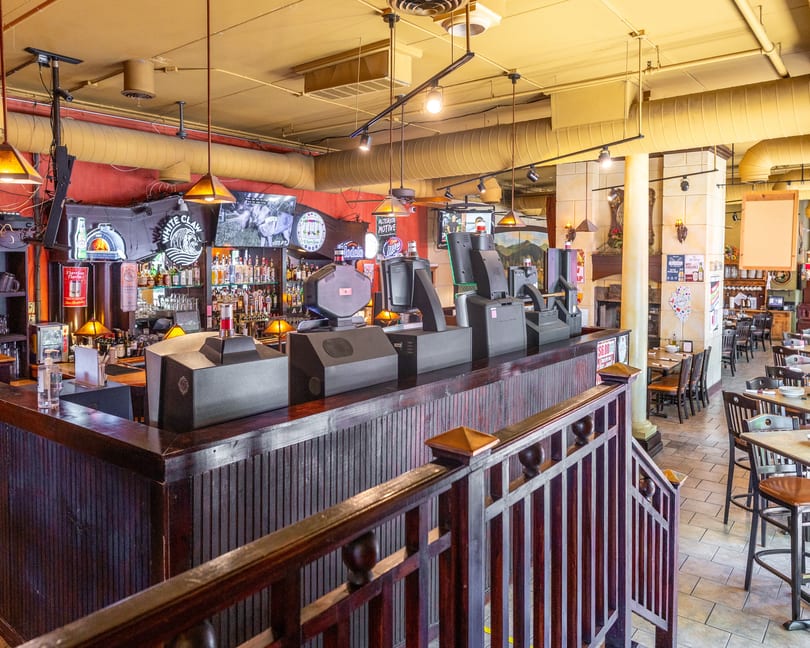 A restaurant interior with a long wooden bar, liquor bottles, TVs, and dining tables.